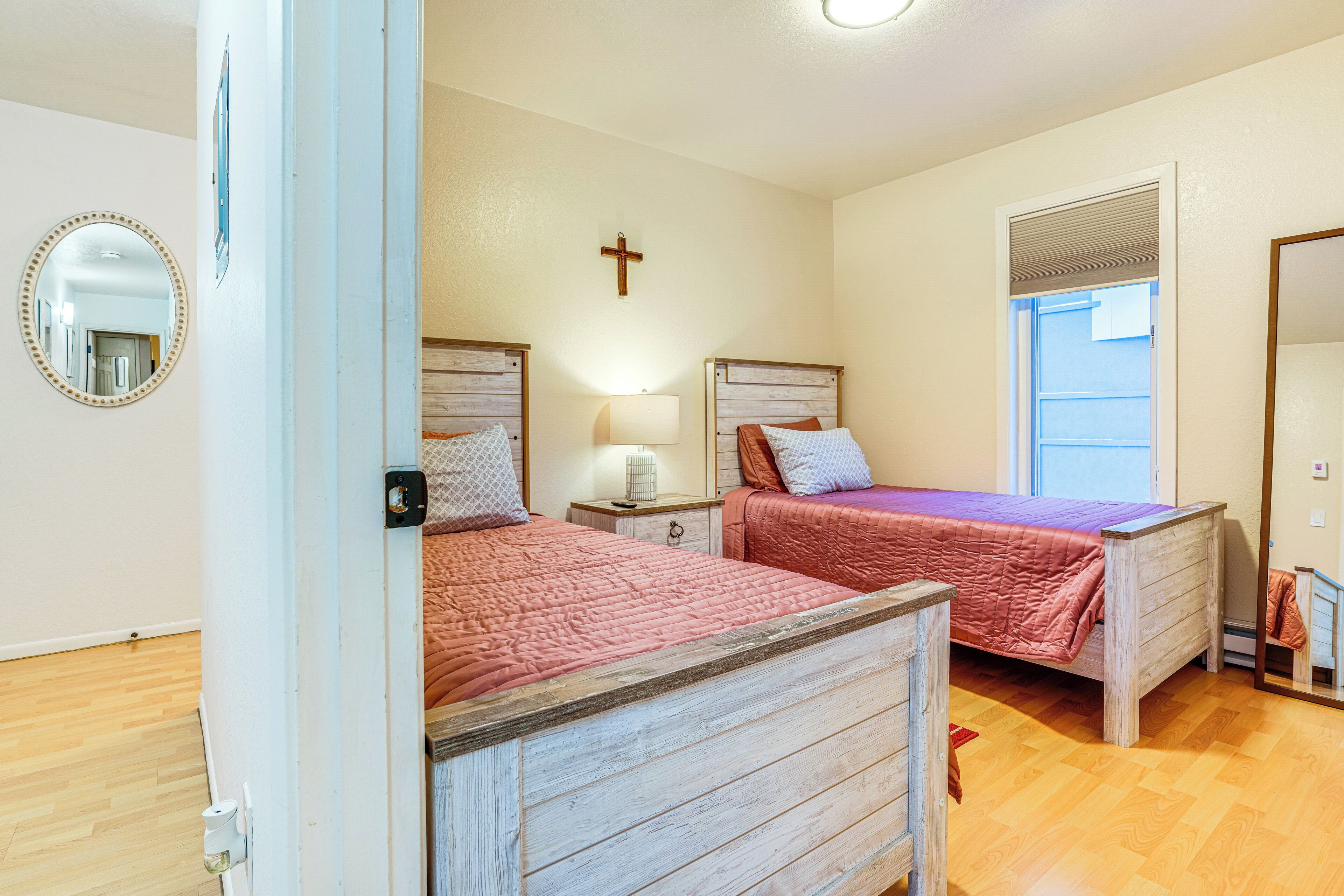 A bedroom with two wooden beds, a nightstand with a lamp, a mirror, and a cross on the wall.