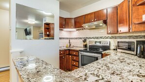 A kitchen with granite countertops, wooden cabinets, a stove, oven, microwave, and a large mirror. - 1 Mi to Dtwn: Cozy Condo in Anchorage! (Anchorage)