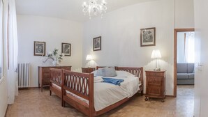 A bedroom with a wooden bed, two bedside tables with lamps, a radiator, and framed pictures on the walls.