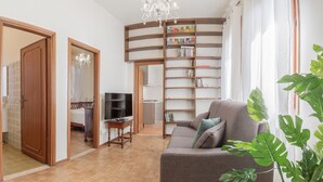 A living room with a sofa, a TV, a bookshelf, and a staircase leading to another room.