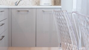 A modern kitchen with grey cabinets, a microwave, a toaster, and a clear chair.