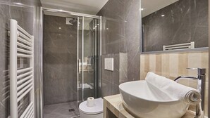 Ein modernes Badezimmer mit einer gläsernen Duschkabine, einem weißen Waschbecken und einem Handtuchhalter.