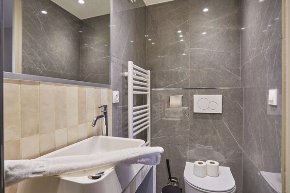 A modern bathroom with a white sink, a towel rack, and two rolls of toilet paper on the wall.
