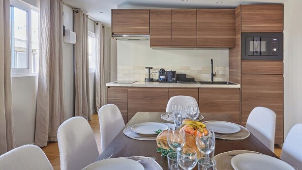 A modern kitchen with wooden cabinets, a built-in microwave, and a dining area set for six with white chairs and a table set for a meal. - Superb Apartment 2 Bedrooms Center of Paris (Paris)