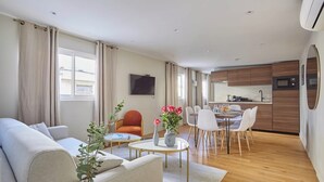 A modern living room with a sofa, a dining table, and chairs, a kitchen area with a microwave and cabinets, and a TV mounted on the wall. - Superb Apartment 2 Bedrooms Center of Paris (Paris)