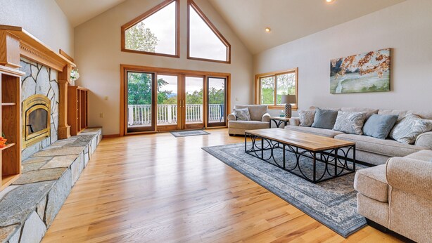A spacious living room with a stone fireplace, wooden flooring, a large sofa set, and a view through the glass doors to the outside. - Vineyard Farmhouse in Oakland w/ Hot Tub! (Oakland)