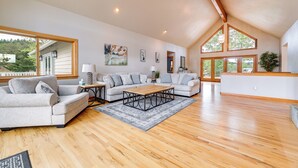 A spacious living room with a large sofa, a coffee table, and a dining table. There are multiple windows providing natural light and a view of the outdoors. - Vineyard Farmhouse in Oakland w/ Hot Tub! (Oakland)