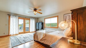 A bedroom with a bed, a desk, a lamp, a ceiling fan, and large windows. - Vineyard Farmhouse in Oakland w/ Hot Tub! (Oakland)