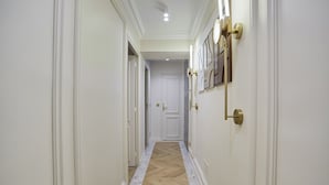 A hallway with white walls, a herringbone-patterned floor, and a door at the end. - Apartment in the Marais With Air-conditioned (Paris)