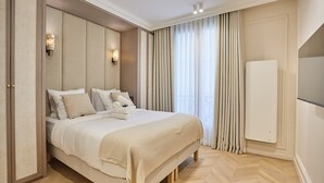 A hotel room with a large bed, a built-in headboard, a radiator, and a large window with curtains. - Apartment in the Marais With Air-conditioned (Paris)