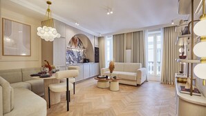 A spacious living room with a herringbone floor, a sofa, a coffee table, and a dining area with chairs. - Apartment in the Marais With Air-conditioned (Paris)