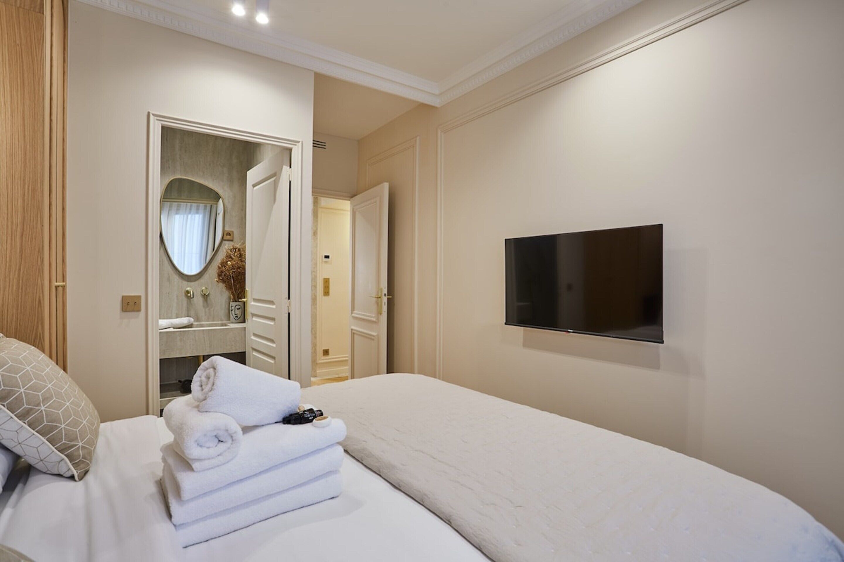 A hotel room with a bed, a TV mounted on the wall, and a bathroom visible through an open door.