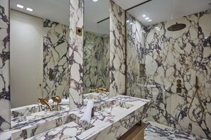 A bathroom with marble walls and a large mirror. There is a sink with a gold faucet and a towel rolled up on the counter. - New/suite Air-conditioned Opera/louvre/ 2 Bedrooms (Paris)