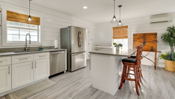 A modern kitchen with white cabinetry, stainless steel appliances, and a wooden island with a bar stool. - 1 Block to Beach: Home w/ Patio in Murrells Inlet! (Murrells Inlet)