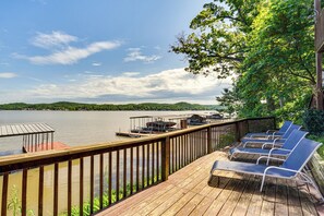 Eine Holzterrasse mit Liegestühlen mit Blick auf einen See, ein Steg mit Booten und ein Gebäude mit Überdachung.
