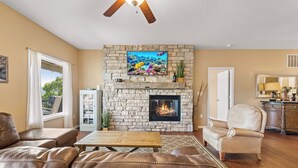 A living room with a stone fireplace, leather sofas, a wooden coffee table, and a television mounted above the fireplace. - Lakefront Ozarks Home: Tiki Bar, Pool, Deck, Views (Camdenton)