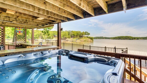 A wooden deck with a hot tub overlooking a lake. - Lakefront Ozarks Home: Tiki Bar, Pool, Deck, Views (Camdenton)