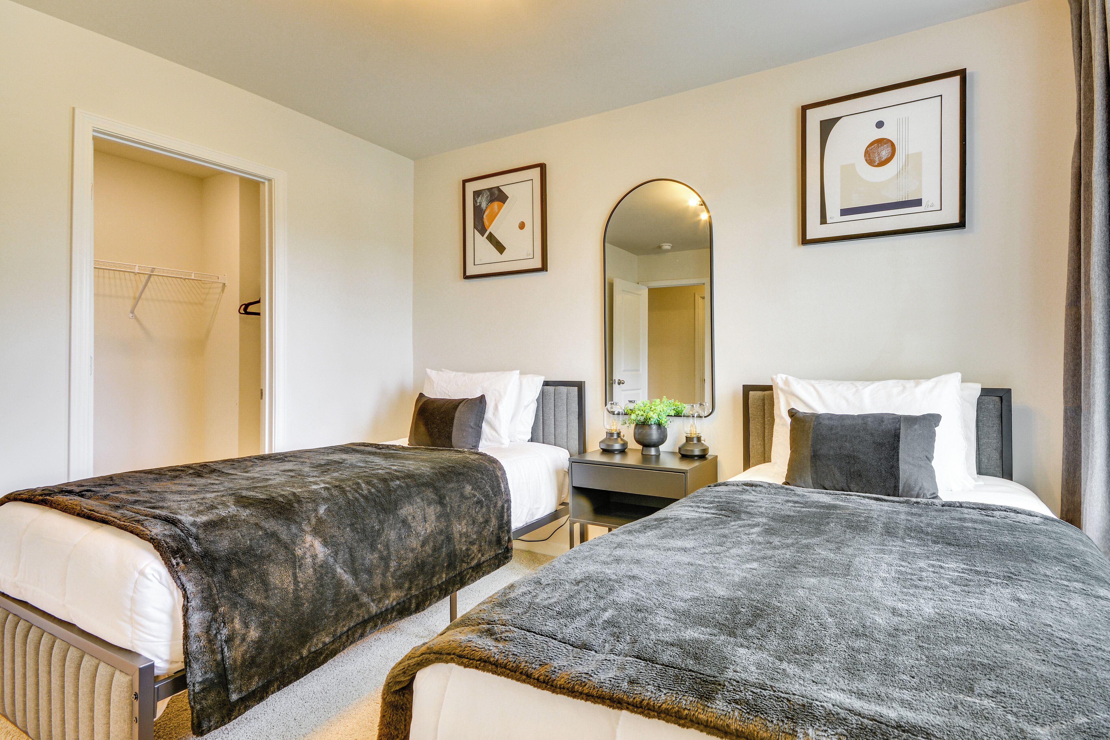A hotel room with two beds, a bedside table with a lamp, a mirror, and artwork on the walls.