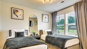 Quarto de hotel com duas camas, um espelho grande e uma janela com cortinas.