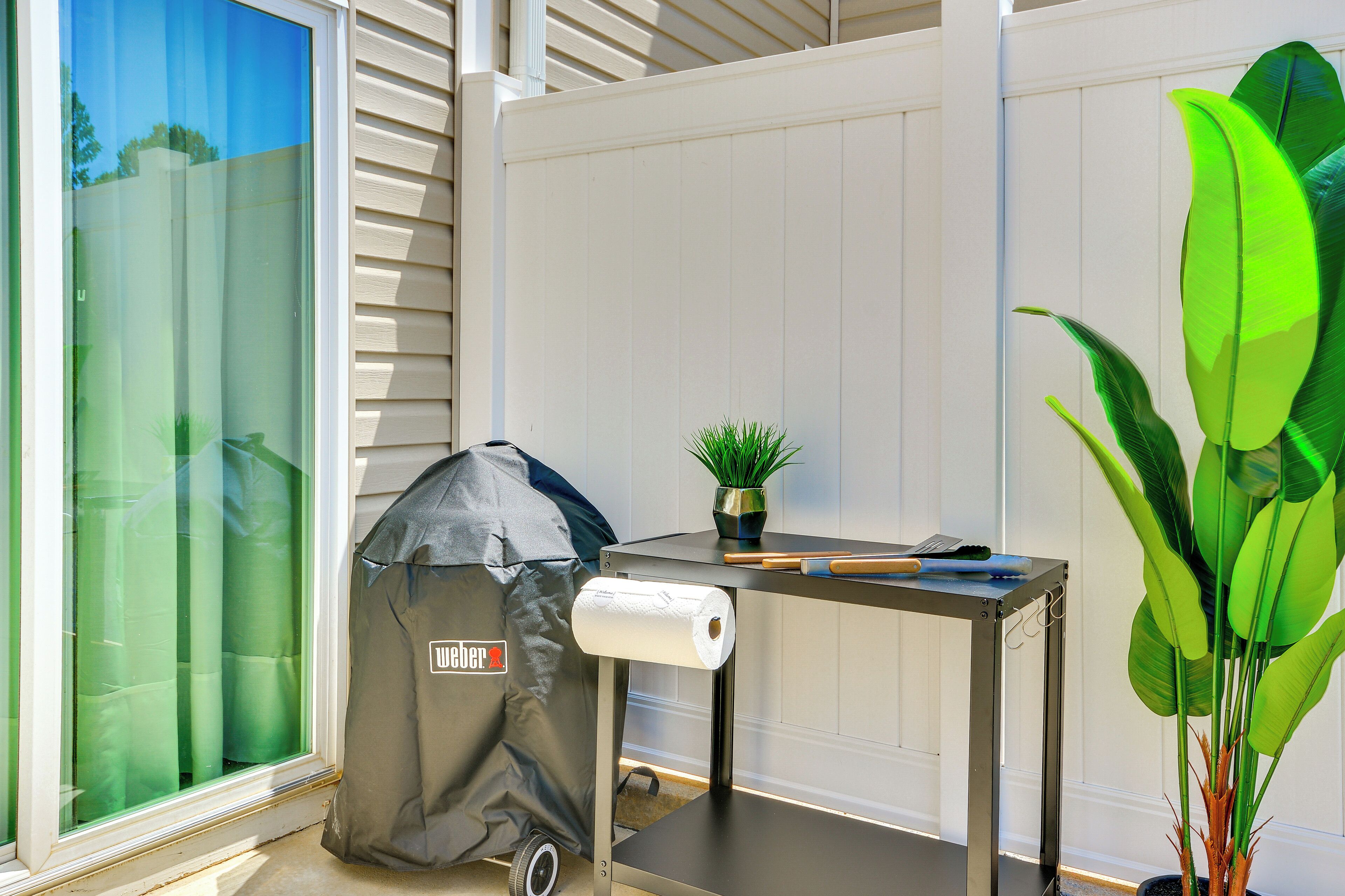 A patio area with a grill, a table with a plant, and a window with blinds.
