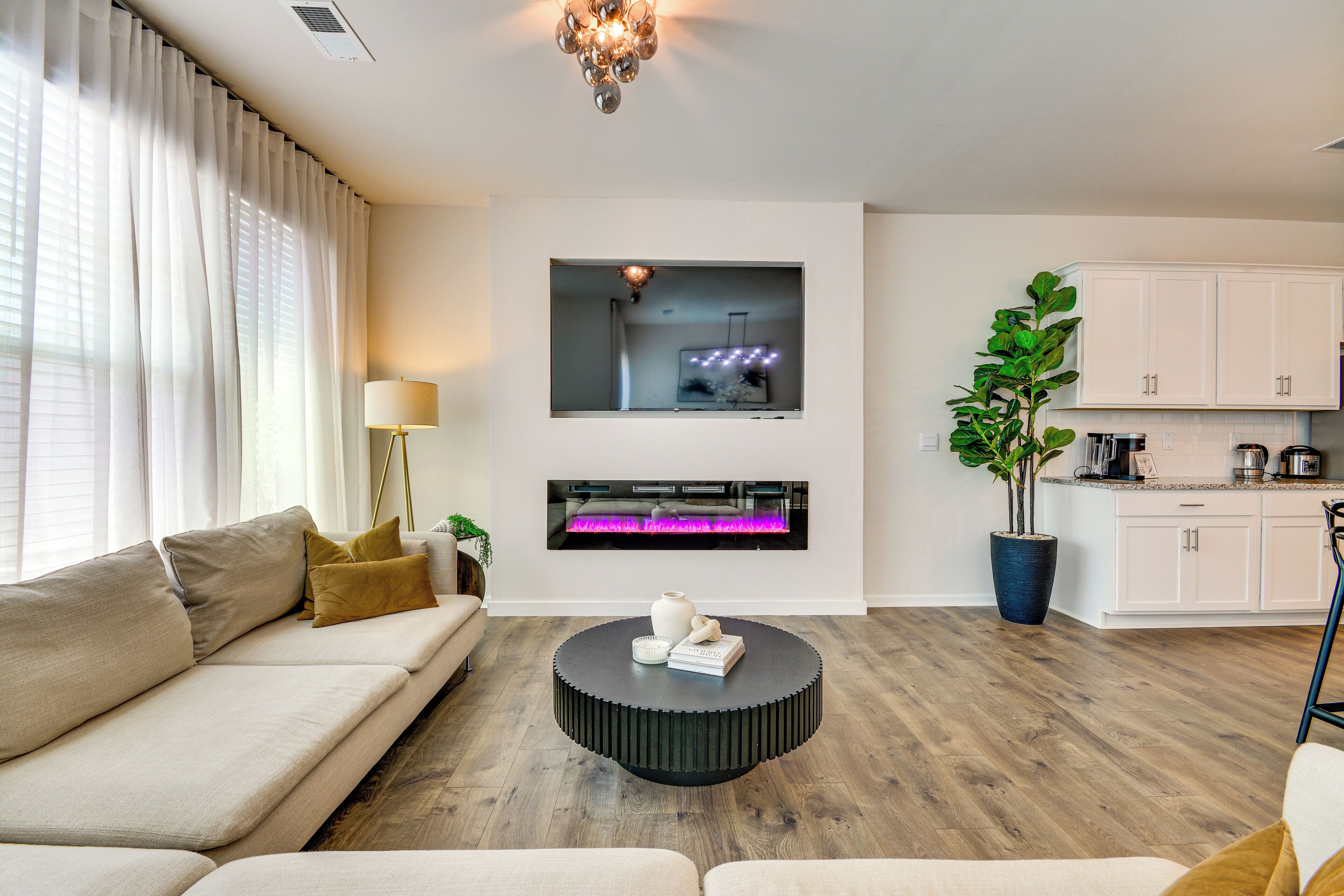 A modern living room with a sofa, a round coffee table, a fireplace, and a kitchen area with cabinets.