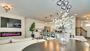 Uma cozinha moderna com armários brancos, uma área de refeições com mesa redonda e uma escada para outro andar.