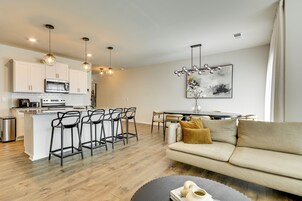 Cozinha moderna com ilha central, banquetas, área de jantar com mesa e cadeiras, e sala de estar com sofá.