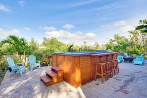 A wooden hot tub with a blue cover, surrounded by outdoor seating including bar stools and chairs, set on a patio with a brick floor and lush greenery in the background. - Dock, Kayaks & On-site Pond: Terra Ceia Home (Palmetto)