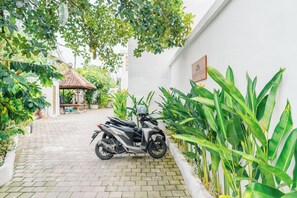 A scooter parked on a paved path beside a white wall with green plants. - 2BR Villa Seminyak with Pool (Seminyak, Badung Regency)