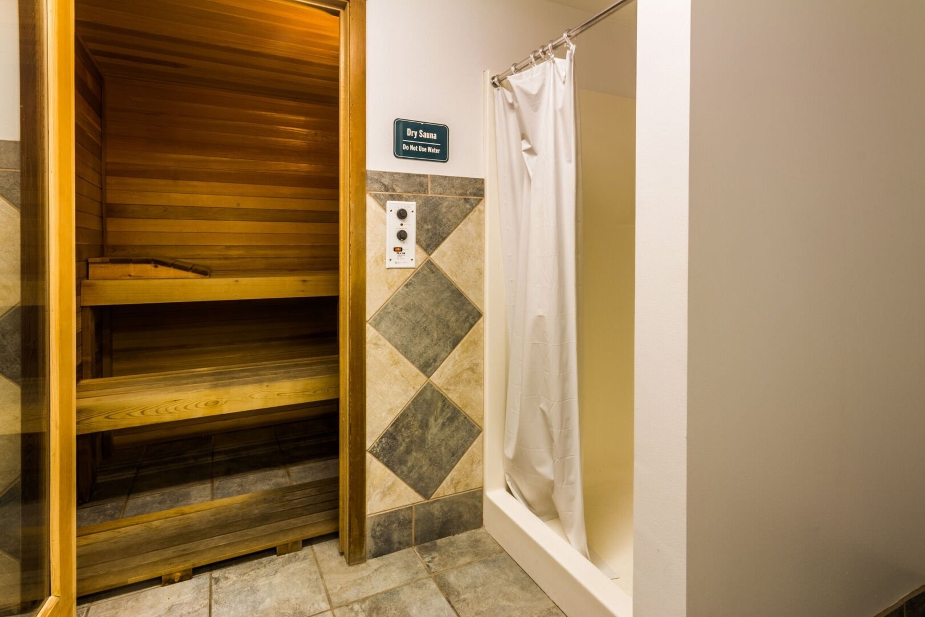 A dry sauna with a wooden bench, a sign instructing not to use water, and a shower curtain.