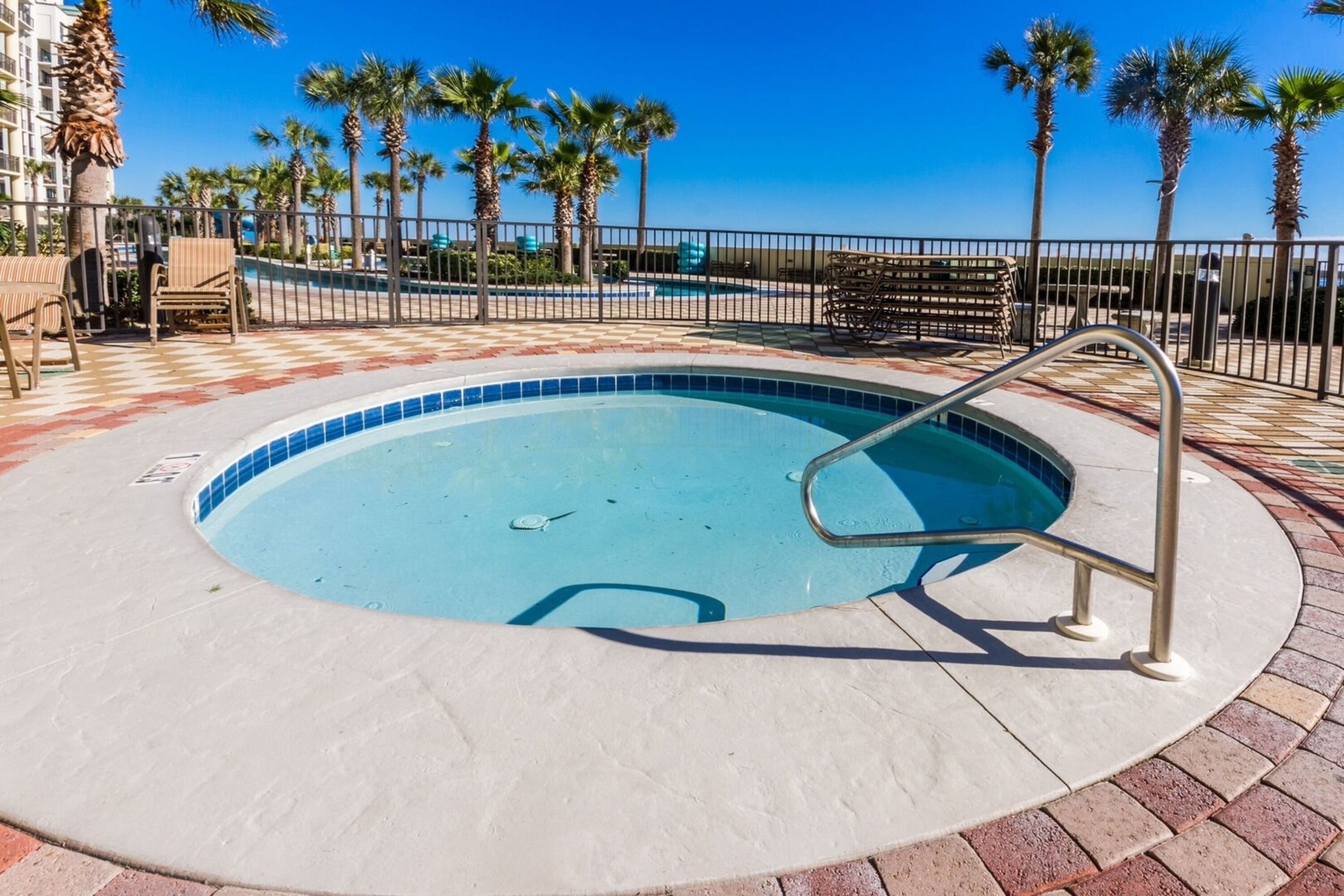 A swimming pool with a metal ladder, surrounded by palm trees and a tiled deck.