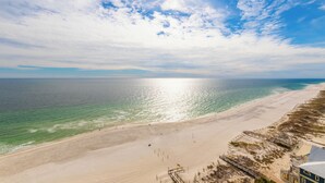 A beach with a wooden walkway leading to a building with a sloped roof. - Phoenix West Condominiums (Orange Beach)