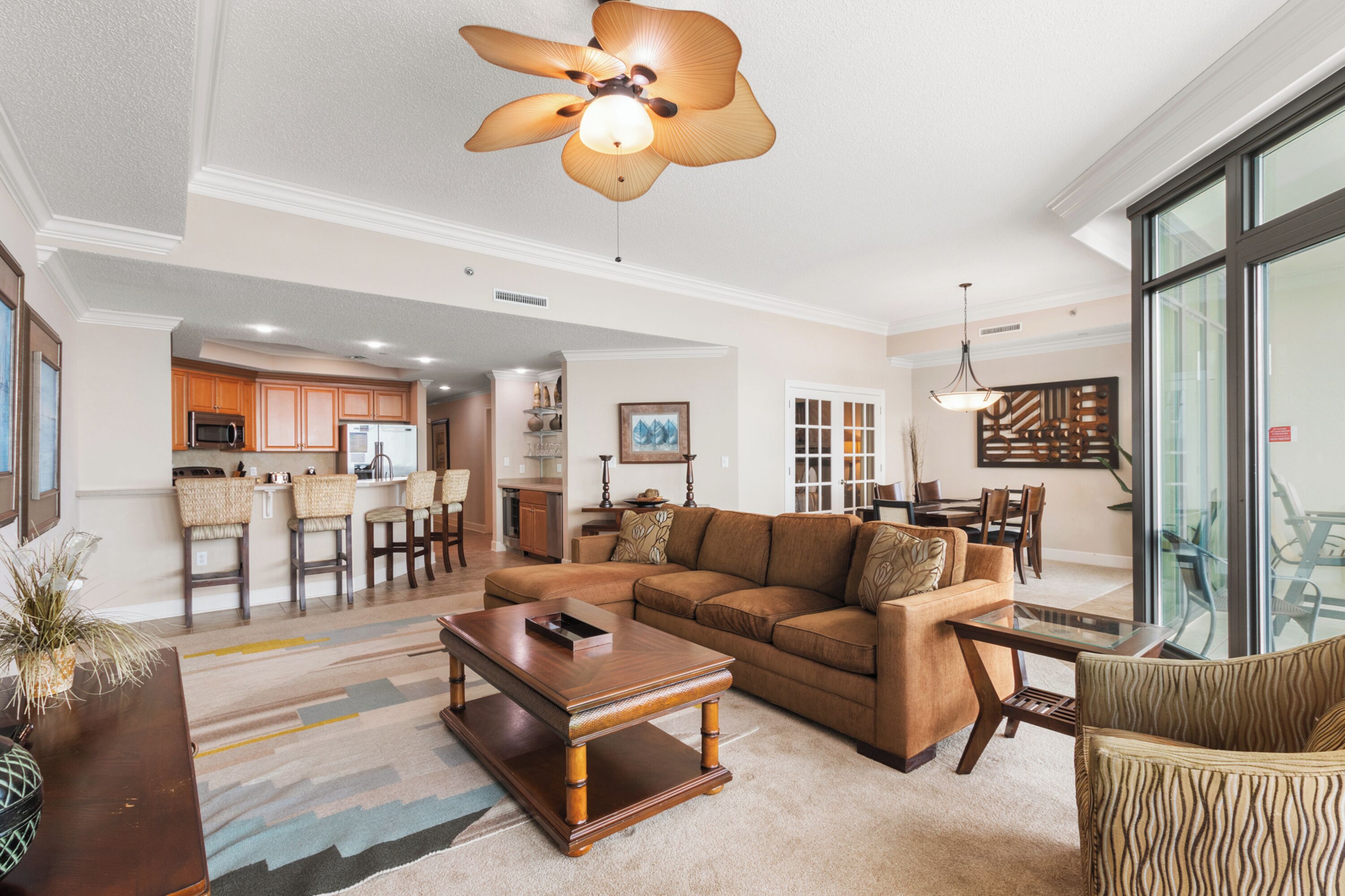 A spacious living room with a large brown sectional sofa, a wooden coffee table, and a ceiling fan.