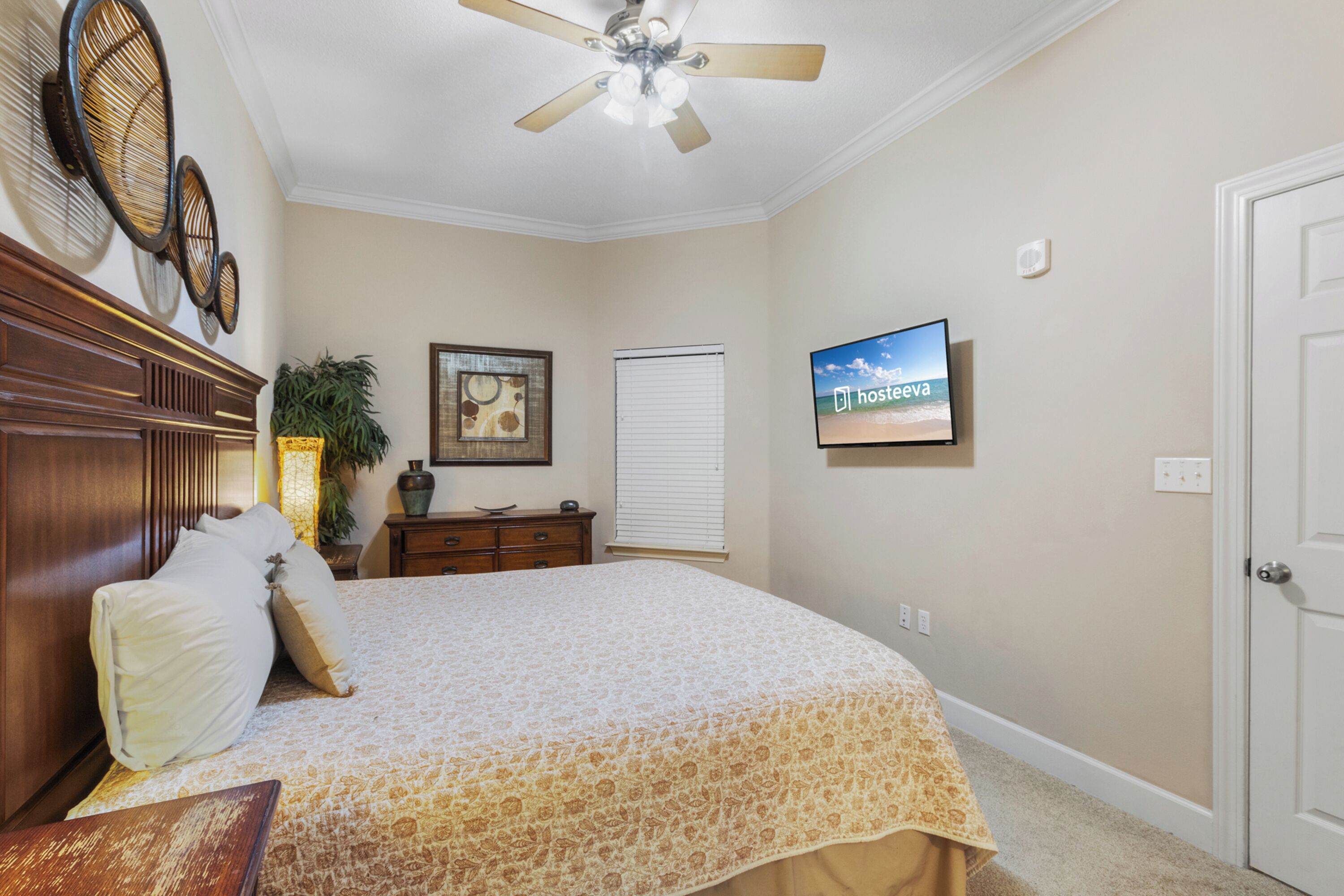 A bedroom with a bed, a ceiling fan, a television, a window with blinds, and a door.