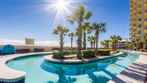 A swimming pool with palm trees and a building in the background. - Phoenix West Condominiums (Orange Beach)