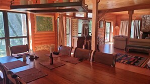 A wooden cabin interior with a dining area, a living room with a sofa, and a stone fireplace. - La Bella Patagonia (Cisnes)
