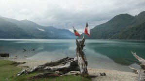 A lake with mountains in the background, a wooden post, and two flags. - La Bella Patagonia (Cisnes)