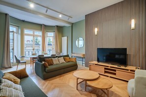 Ein modernes Wohnzimmer mit einer Couch, einem Fernseher und einem Essbereich mit Tisch und Stühlen.