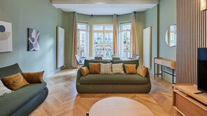 Ein modernes Wohnzimmer mit einem grünen Sofa, einem Esstisch und großen Fenstern.
