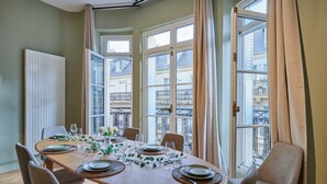 Ein Essbereich mit einem runden Tisch, gedeckt für sechs Personen, großen Fenstern mit Vorhängen und Blick auf die Stadt.