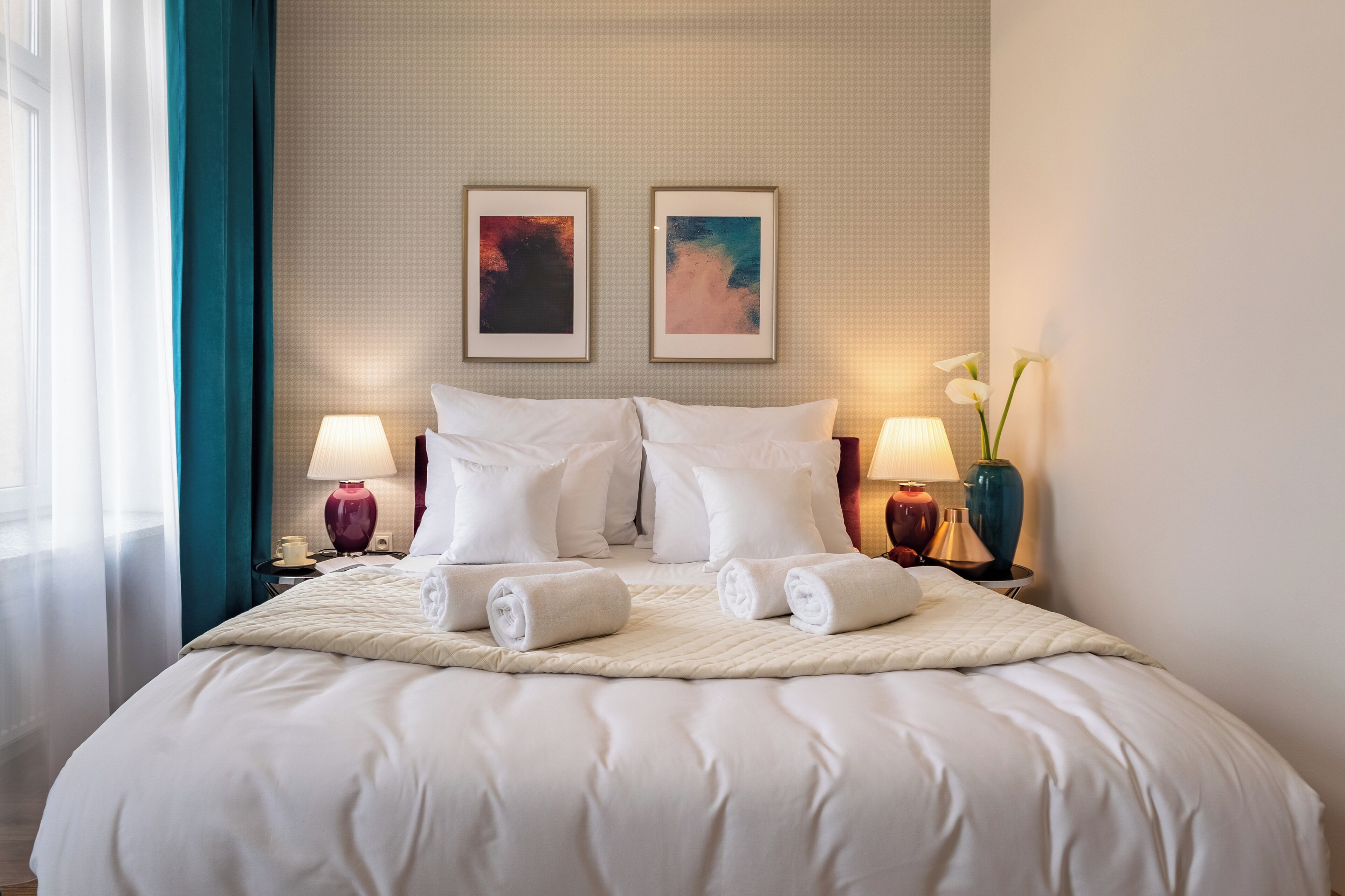 A neatly made bed with white linens and pillows, two framed artworks on the wall, and bedside lamps.