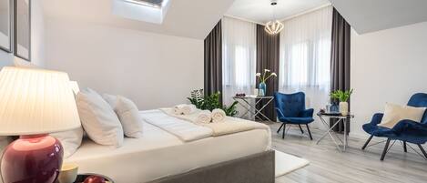 A modern hotel room with a bed, a desk, two chairs, a lamp, and a tray of fruit.