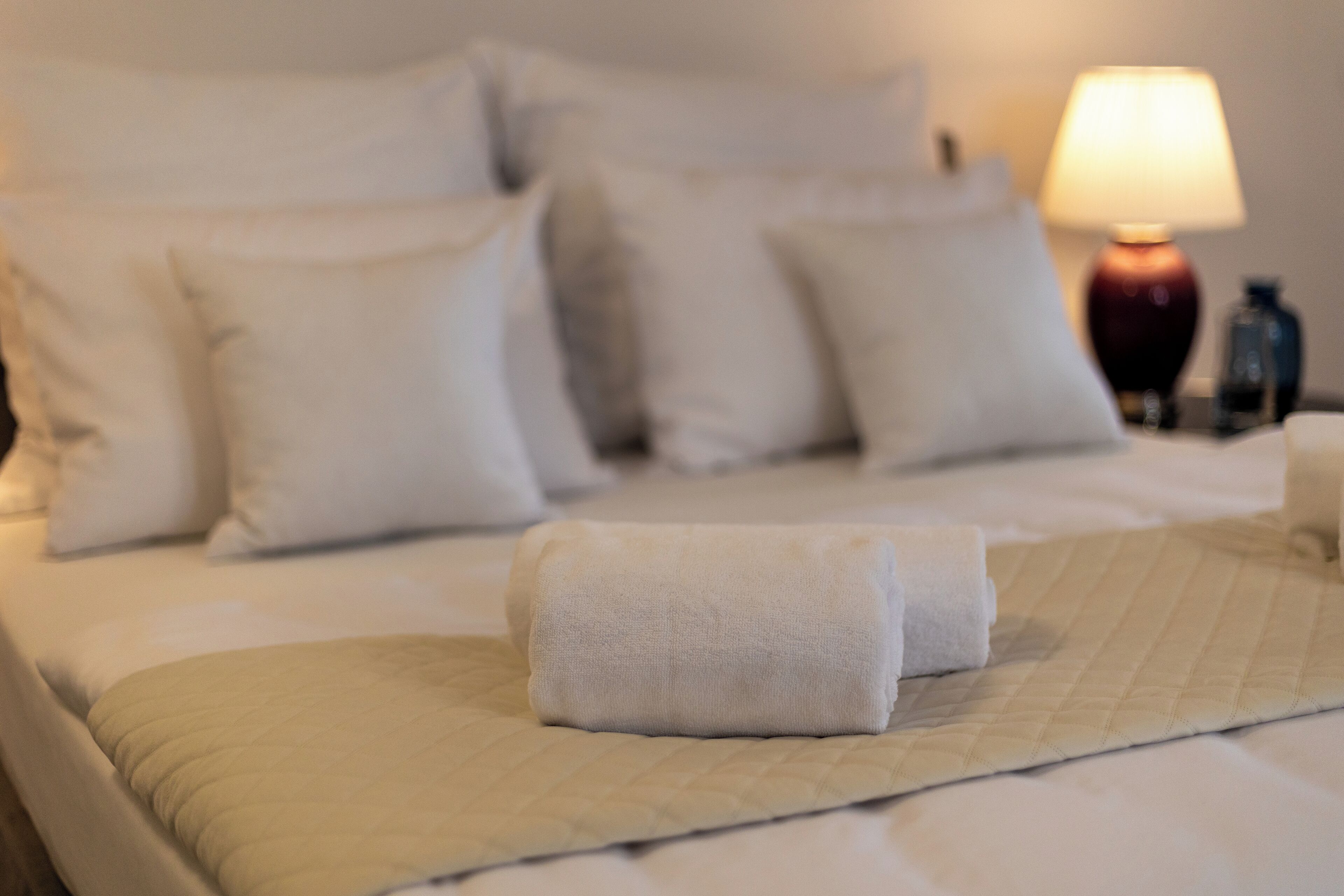 Un letto rifatto con lenzuola bianche e un asciugamano piegato sul comodino.