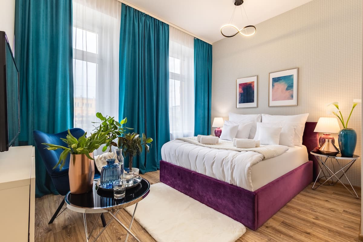 A modern hotel room with a large bed, a desk, a chair, and a potted plant.