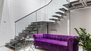 Un interior moderno con un sofá púrpura, una escalera de cristal y una planta en maceta.