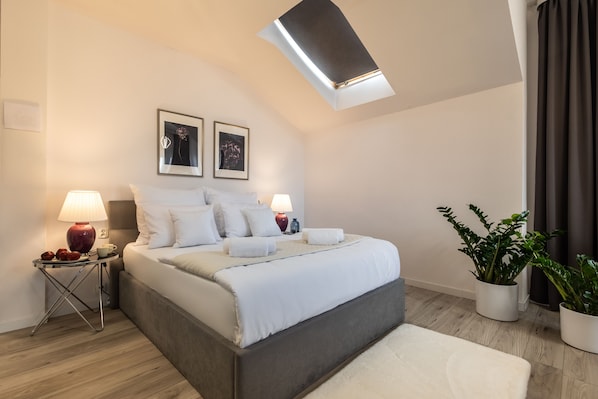 Une chambre moderne avec un grand lit, deux lampes de chevet, une lucarne et deux tableaux encadrés au mur.