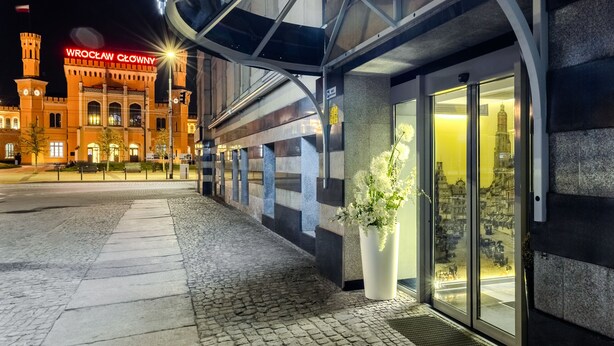 Entrada de hotel con un letrero que dice "SOFIA" y una gran estructura iluminada que parece un castillo al fondo.
