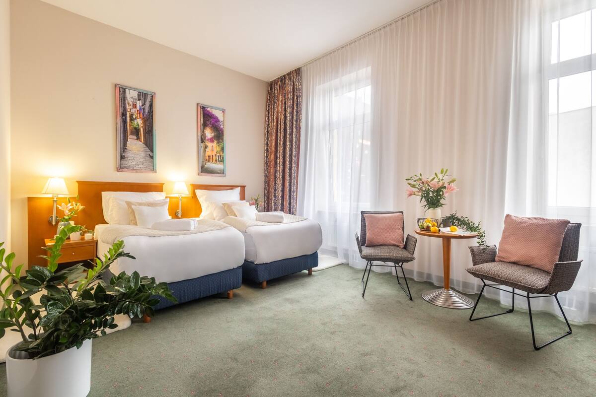 A hotel room with two beds, a sitting area with a table and chairs, and a large window with sheer curtains.