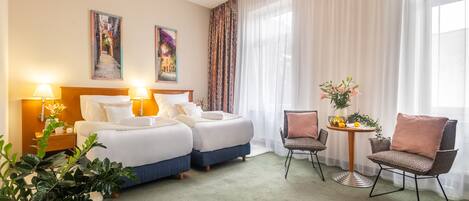 Een hotelkamer met twee bedden, een zithoek met een tafel en stoelen, en een groot raam met dunne gordijnen.