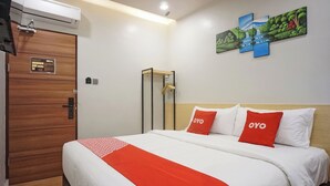 A hotel room with a wooden door, a bed with white and red bedding, and a wall-mounted artwork. - OYO 92956 Travelbiz Hotel (Medan)